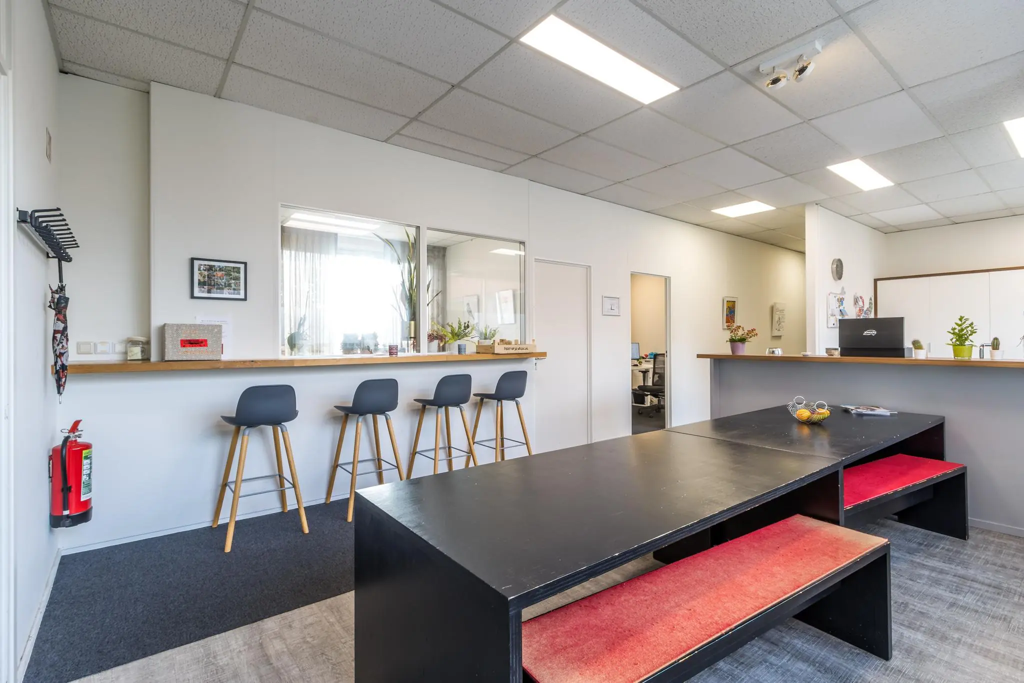 Moderne kantoorruimte aan de Jan van Eycklaan met zithoek, barstoelen en een gemeenschappelijke tafel met rode banken.